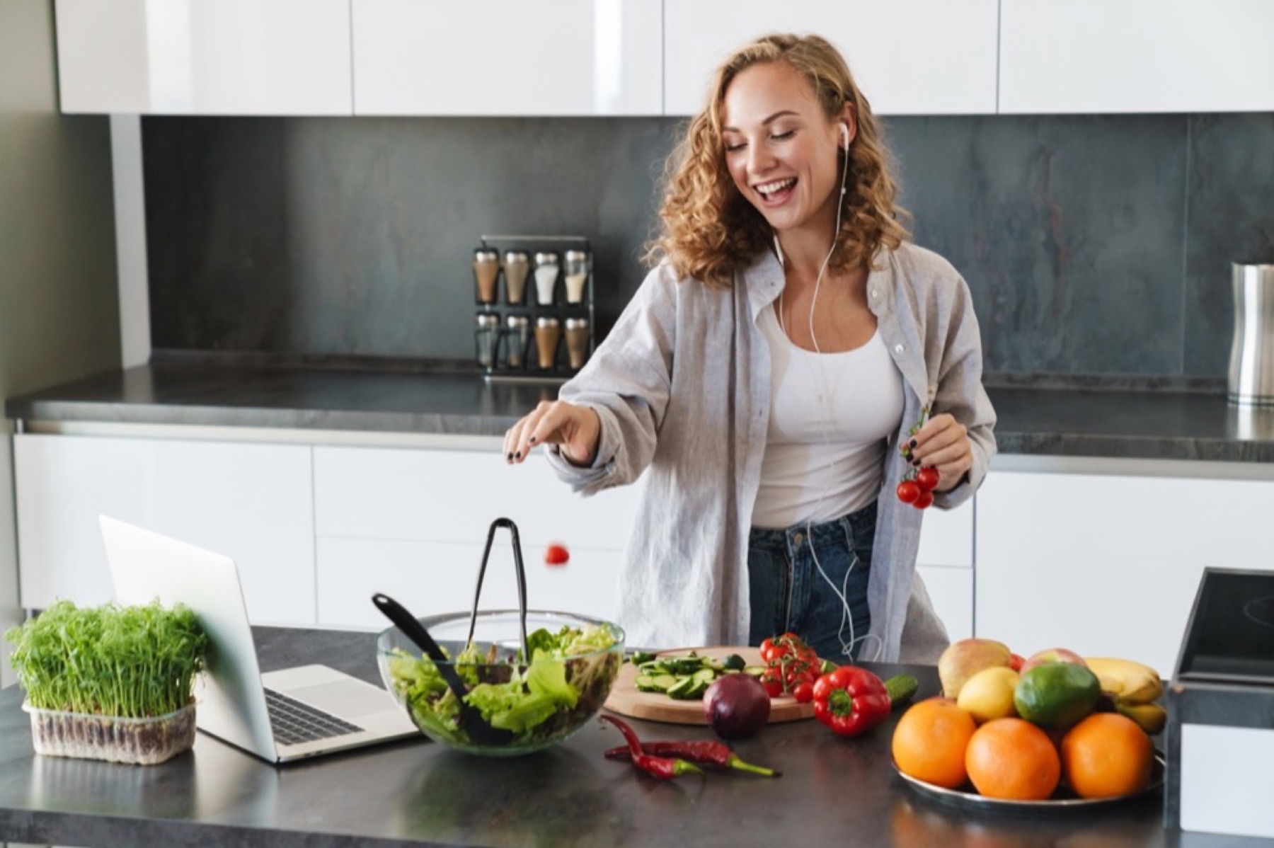 A smiling woman making a salad while listening to music